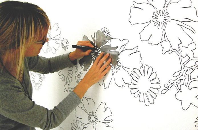 woman painting flowers on the wall using a stencil