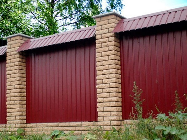 Burgundy fence made of corrugated sheet metal with a ridge